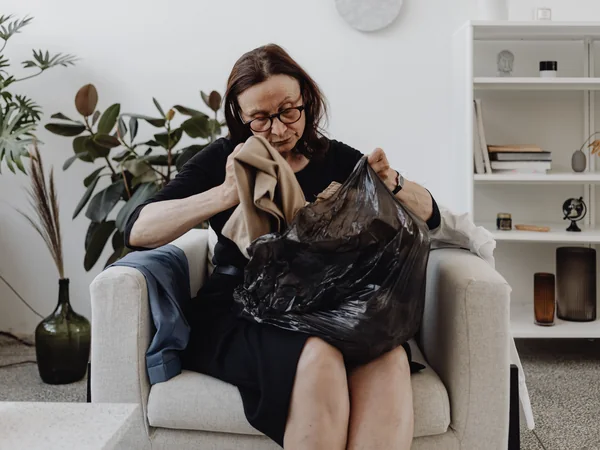 A woman sorting clothing into a removal bag during a household decluttering project
